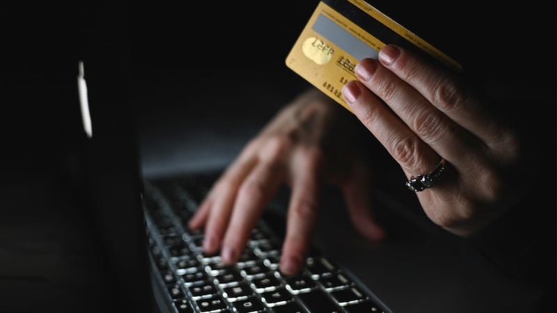 A person sitting at a computer holding a credit card.