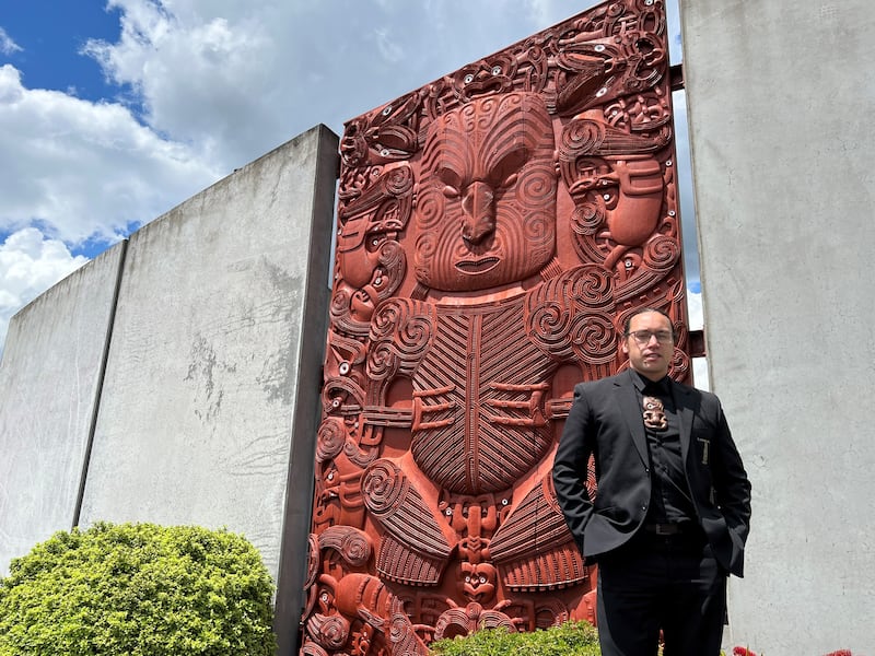 Newly appointed Tumu Whakairo Rākau Grant Marunui stands by a tōtara pou whakairo—one of three he led in design—showcasing the Ngāti Whakaue style, reflecting his iwi, at NZMACI’s entrance.